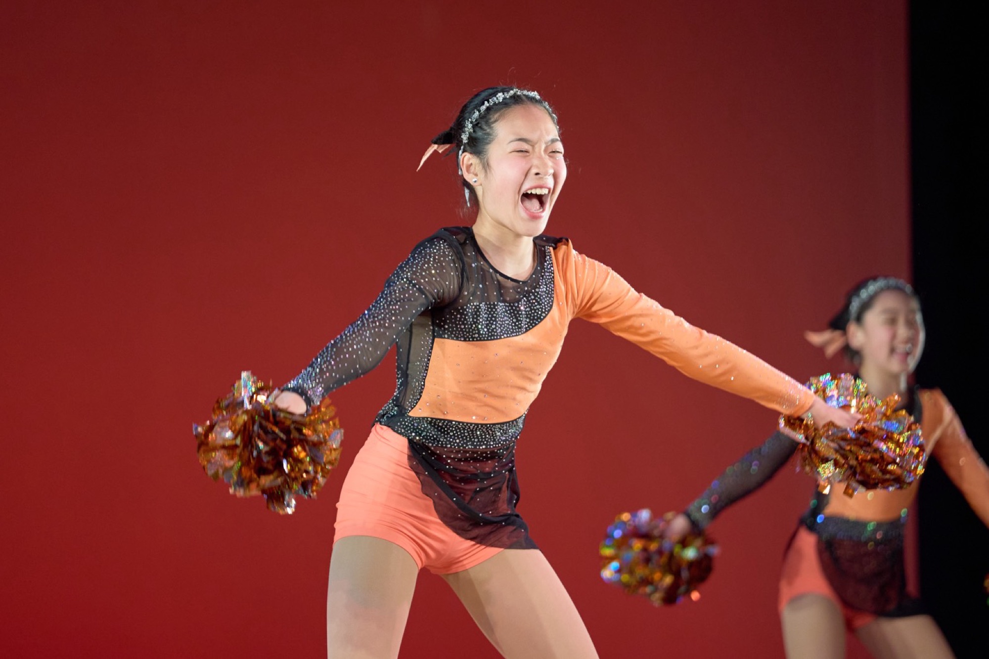 オレンジの衣装で笑顔いっぱいに踊るダンサーたち